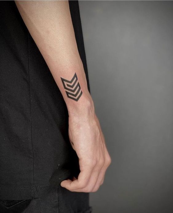 A minimalist tattoo of a small and simple arrow shape on the wrist, representing strength and stability.